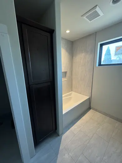 Tall linen cabinets and vanity cabinetry beside the tiled bathing area, view 4.