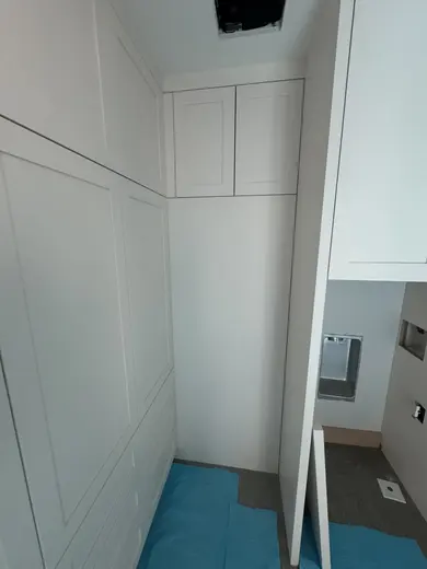 White cabinetry fitted around utility equipment and appliance openings, view 1.