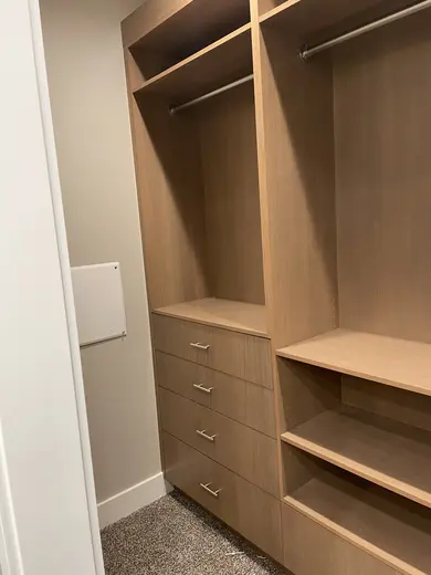 Walk-in closet fitted with natural-wood shelves, drawers and hanging rails.