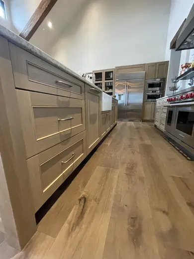 Low-angle view along shaker kitchen cabinets beneath a farmhouse sink and range.