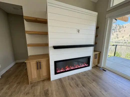 White shiplap fireplace surround with natural-wood shelves and cabinets; exposed media wiring indicates ongoing fit-out.