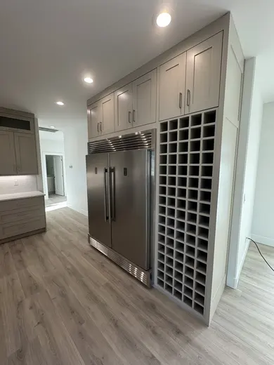 Gray floor-to-ceiling kitchen cabinetry surrounding a stainless refrigerator with a tall wine-bottle grid.