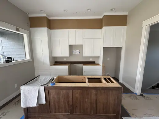 White kitchen cabinetry, a dark wood island and crown installation details, view 5.