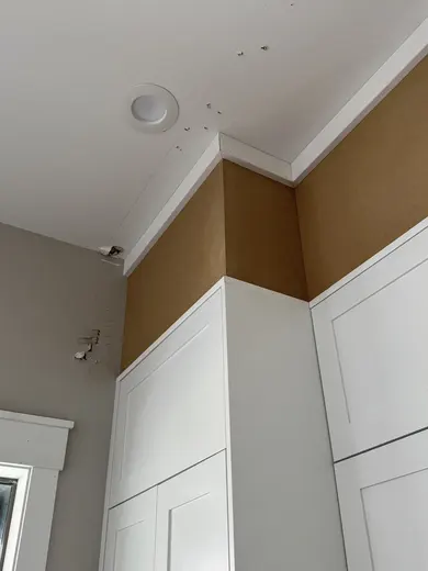 White kitchen cabinetry, a dark wood island and crown installation details, view 7.