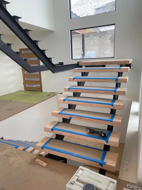 Wood stair treads being installed on a black steel staircase