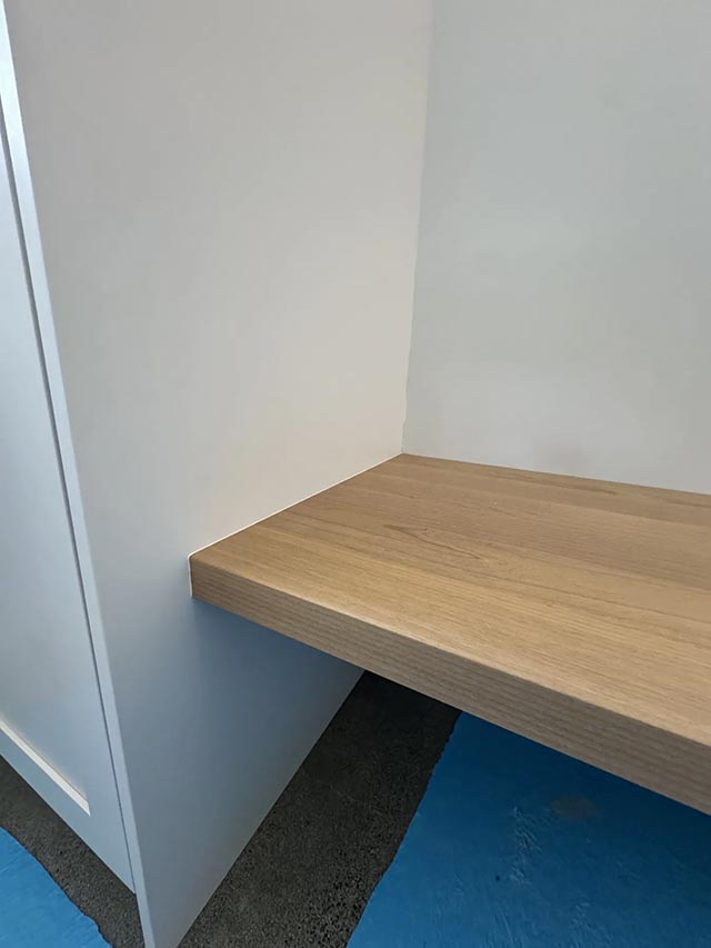A wood seat and floating shelf in a window-side niche, view 2.